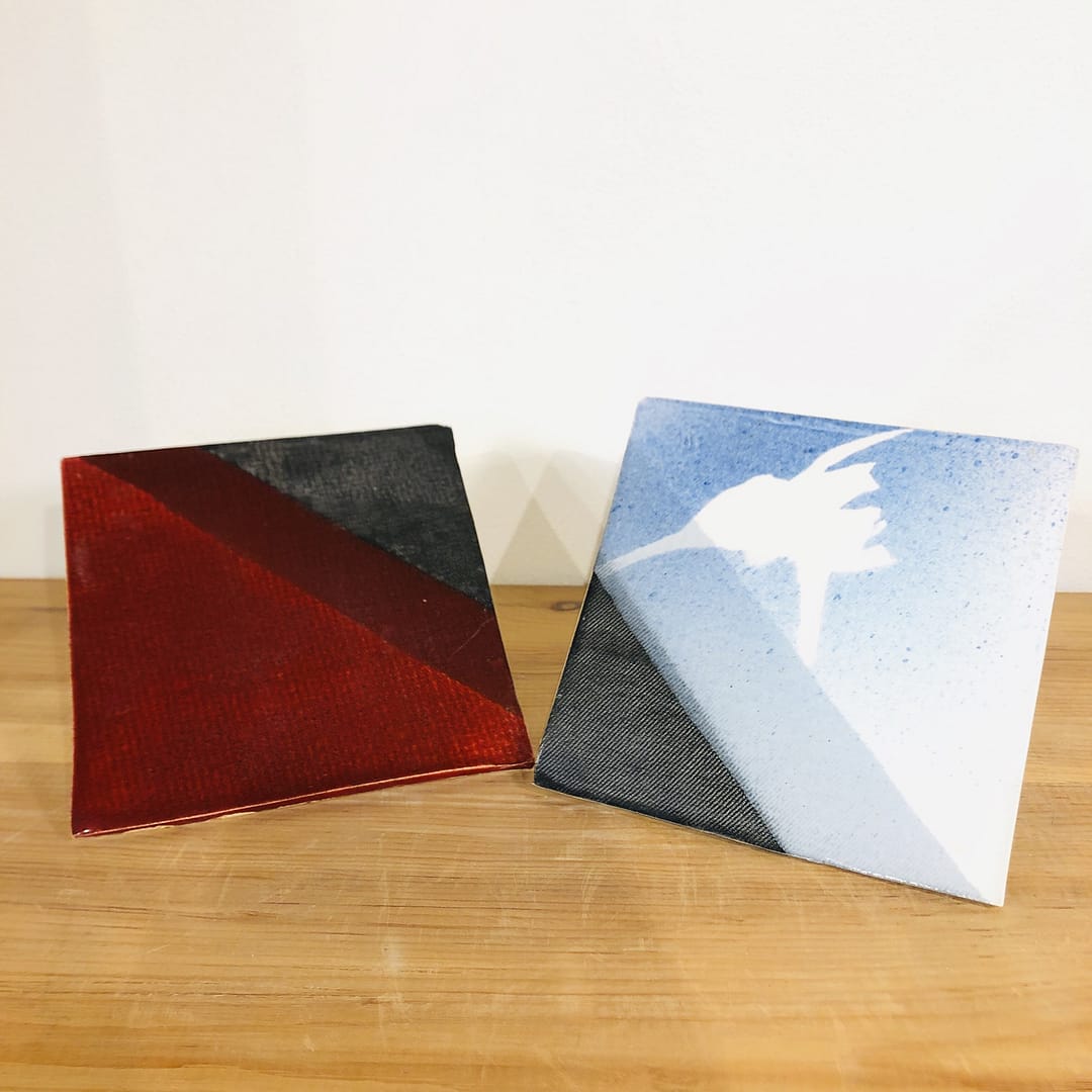 One tile glazed with firebrick red and black, and another with black and blues. The glazes are dipped to form stripes