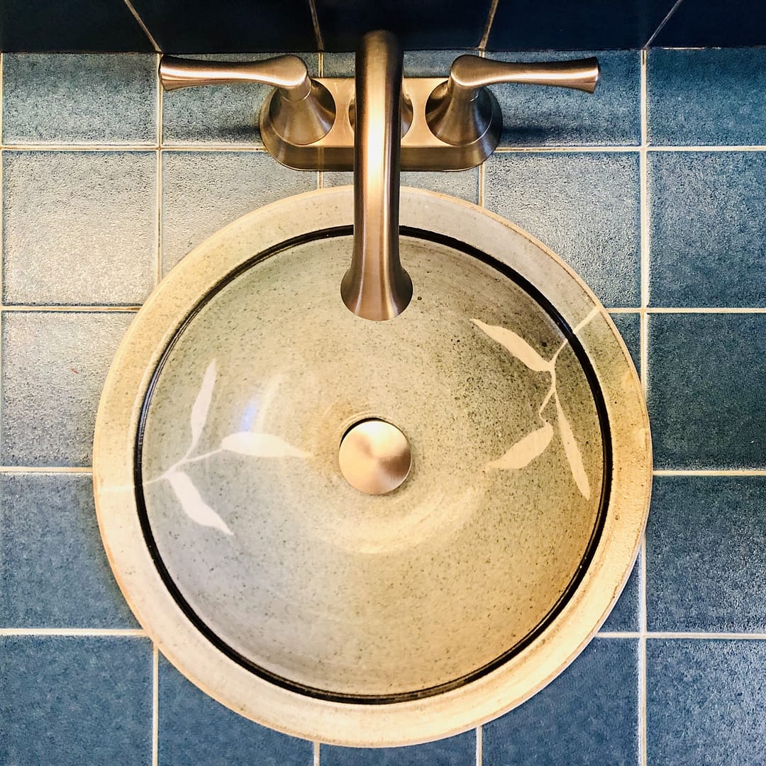 A bathroom sink. It is glazed in turquoise with a leaf stencil pattern