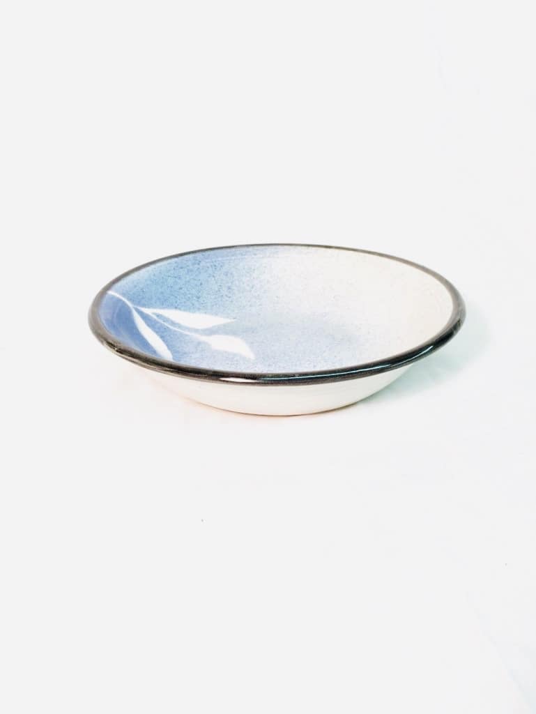 A bowl glazed with blues and a black rim. It has a leaf stencil pattern