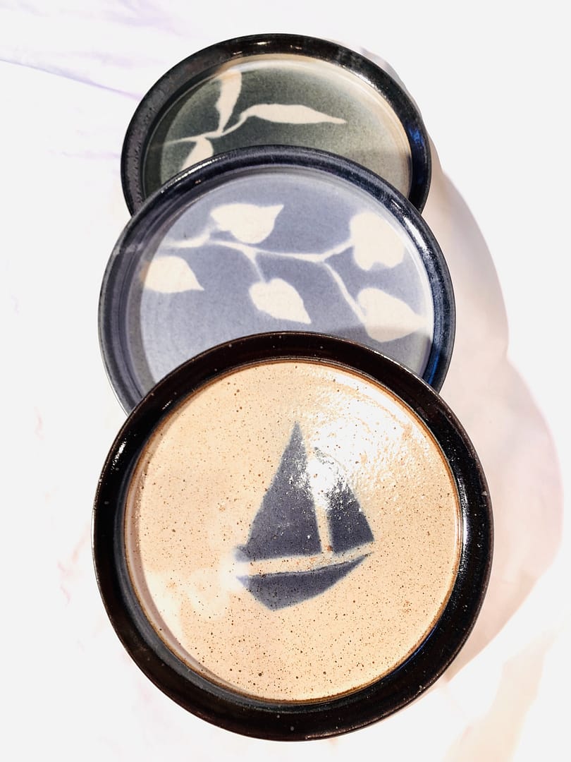 3 salad plates. One is neutral with a blue sailboat, the others are blue and turquoise with a stenciled leaf